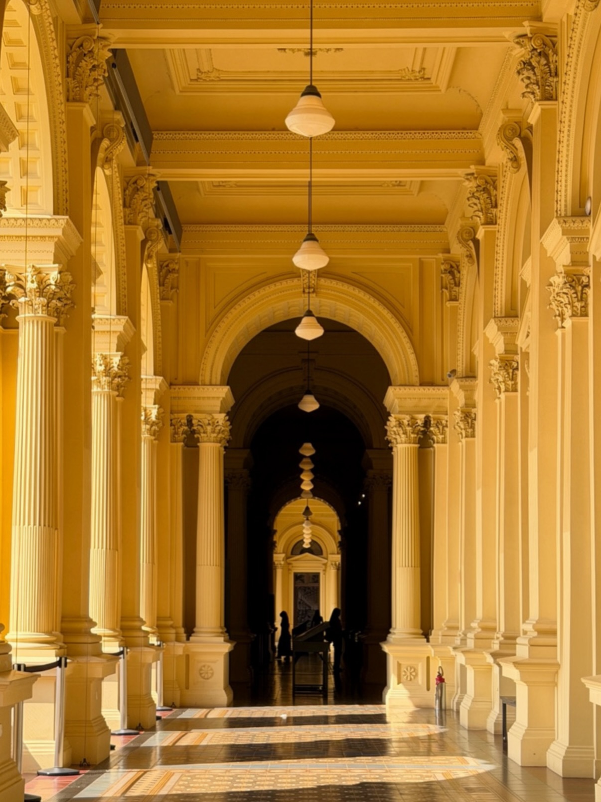 Sunlit yellow neoclassical arcade with pendant lights and columns