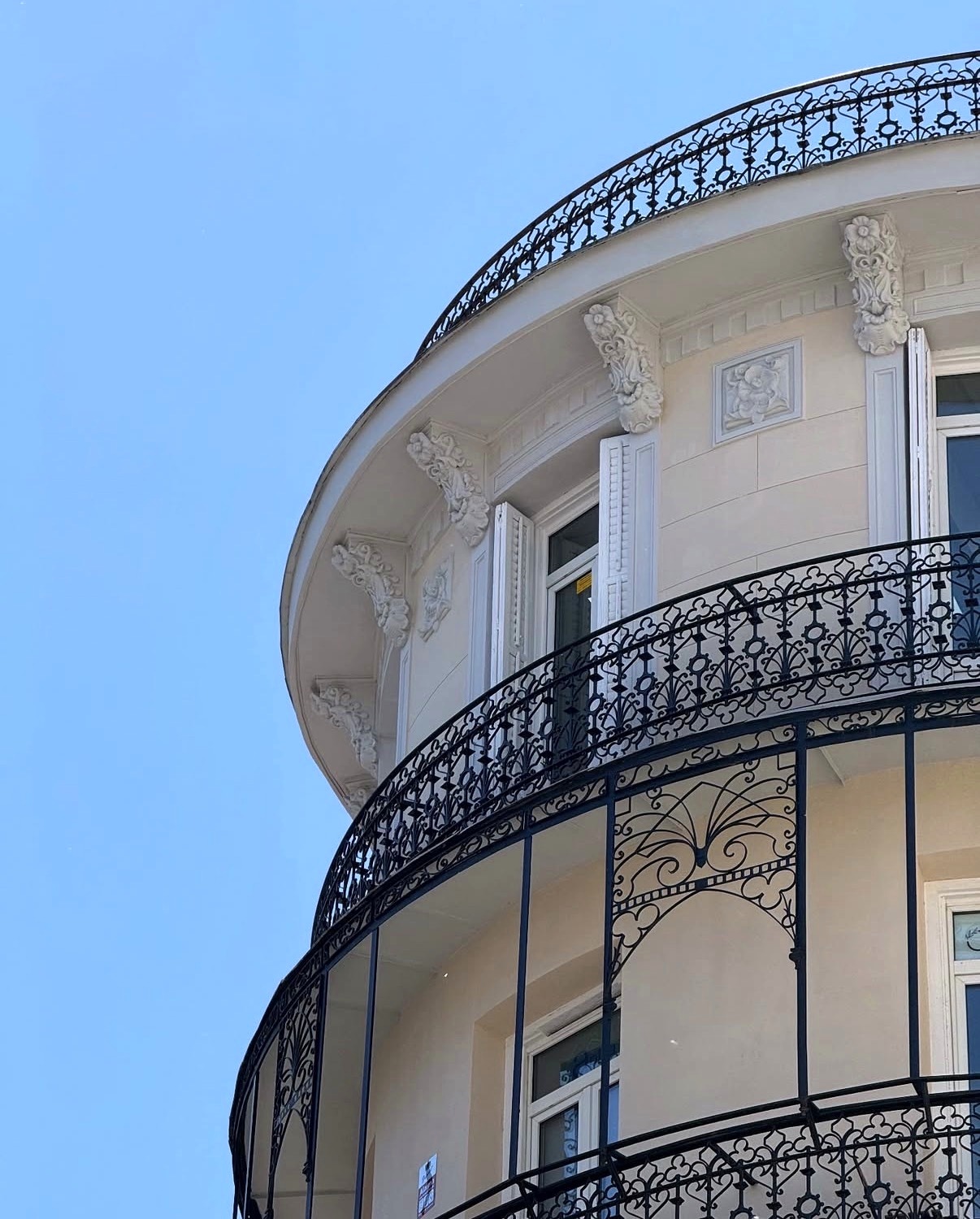 Curved wrought-iron balcony on a cream neoclassical building against a clear blue sky
